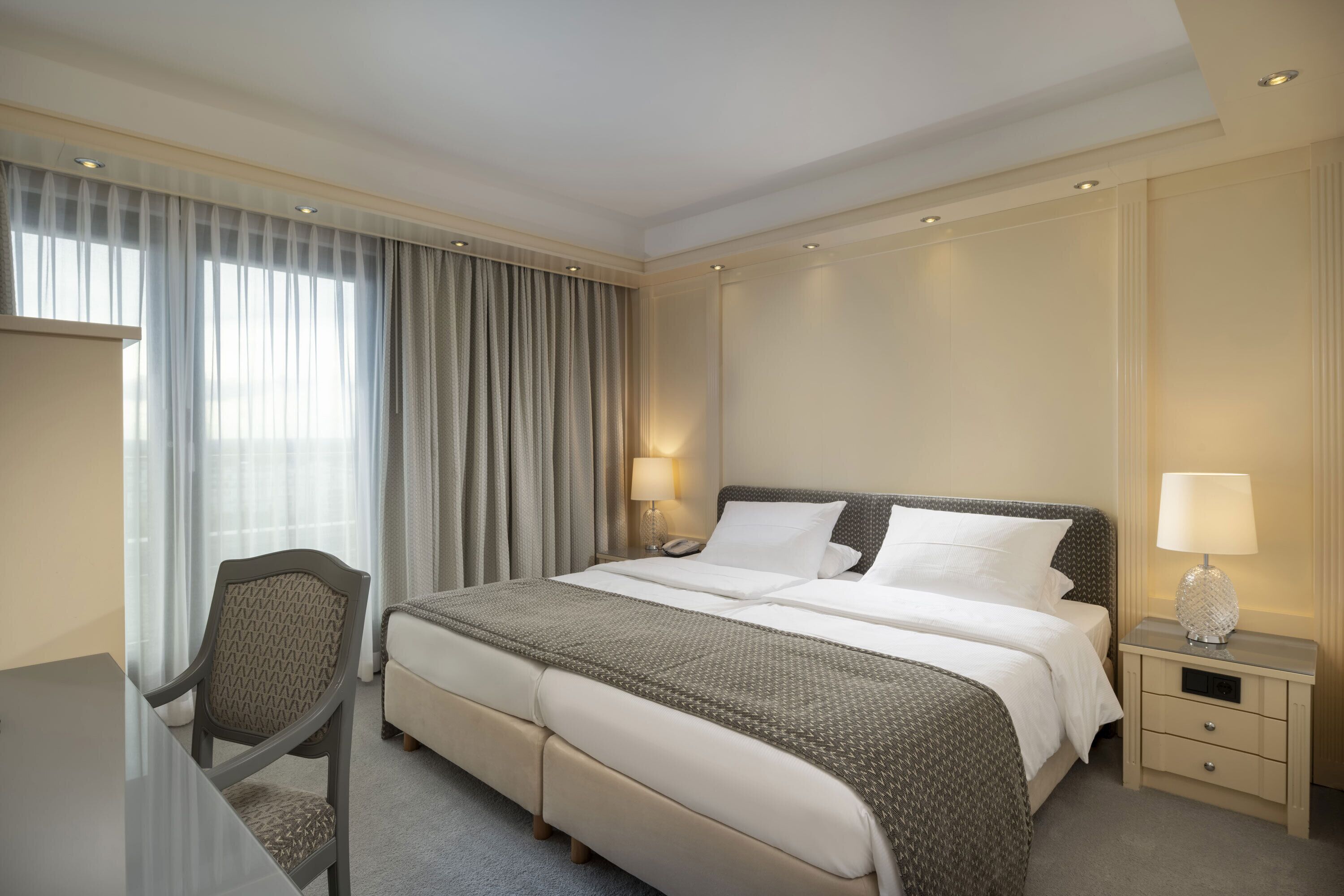 A hotel room with a bed, bedside tables, a desk, and a chair.