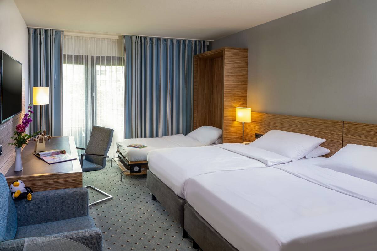 Habitación de hotel con dos camas, un escritorio con lámpara, una silla y un televisor.