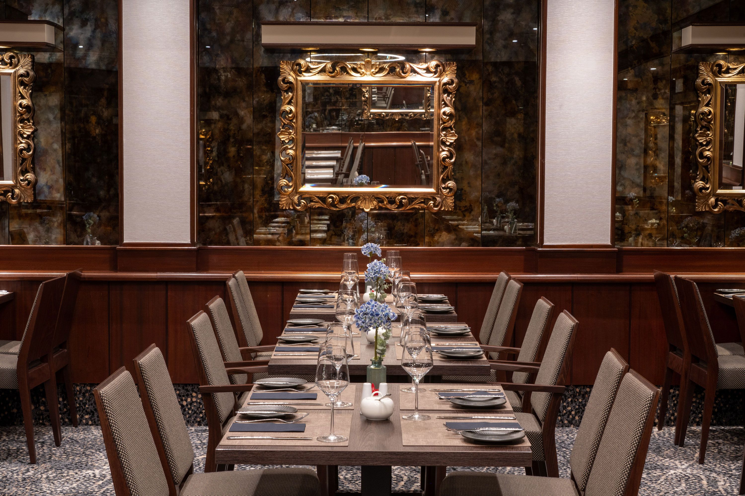 A formal dining room with a long table set for a meal, surrounded by upholstered chairs.