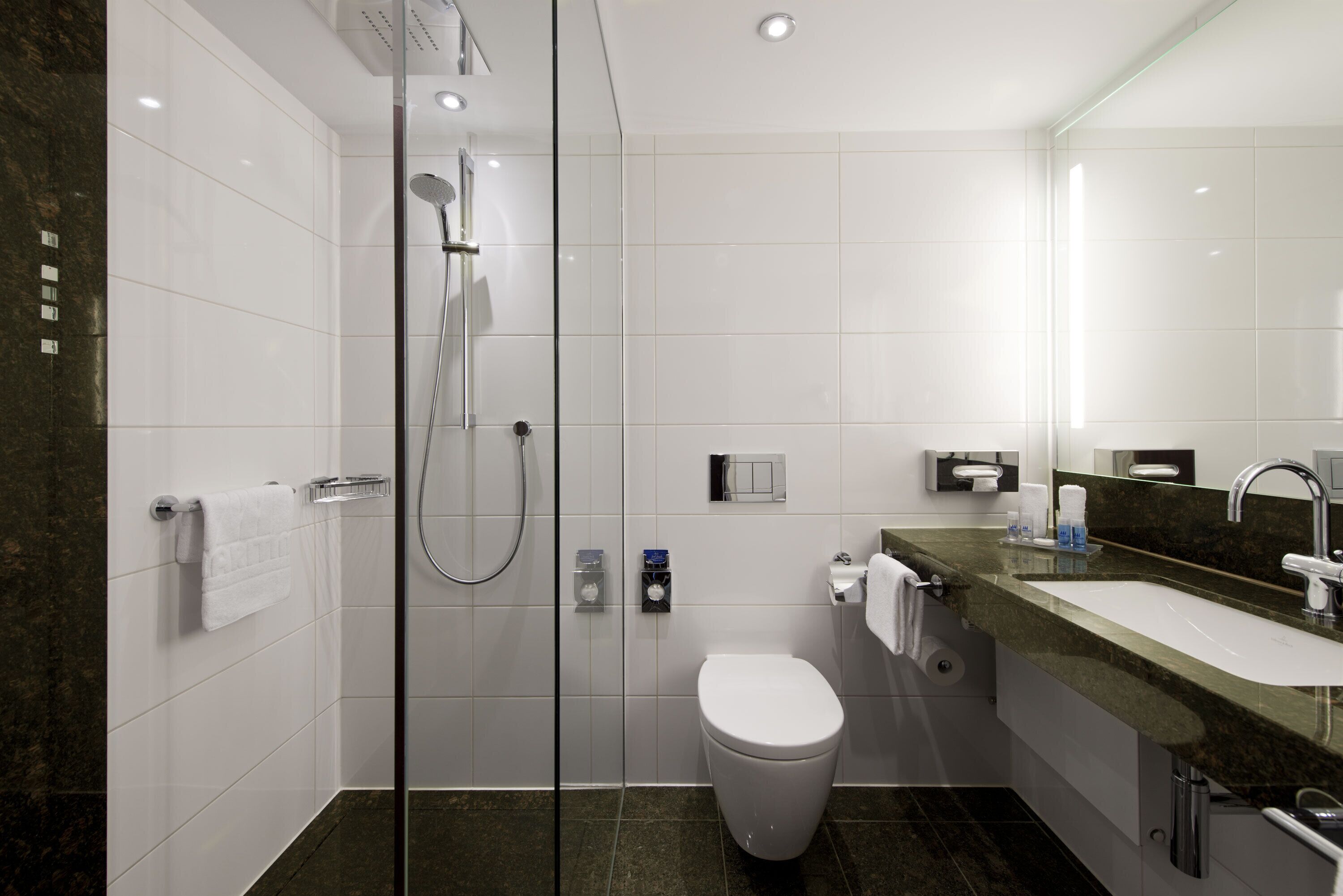 A modern bathroom with a glass-enclosed shower, a white toilet, and a sink with a marble countertop.