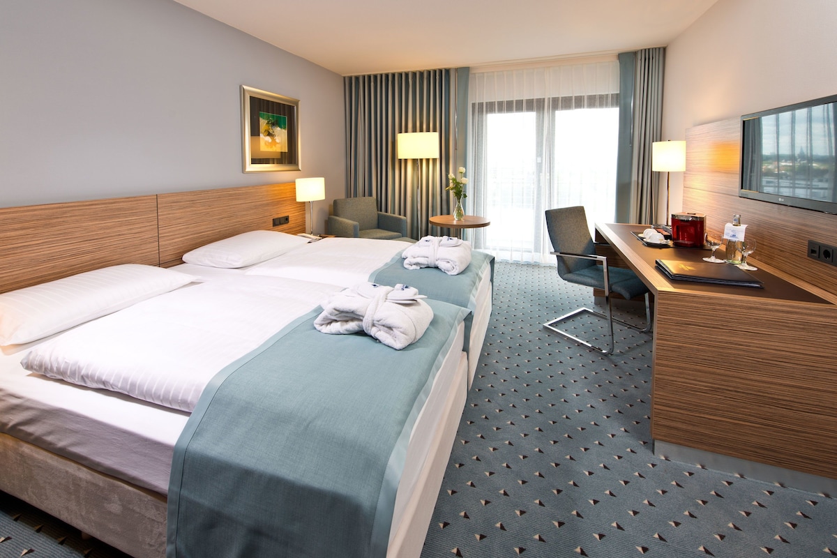A hotel room with two beds, a desk, a chair, a TV, and a window with curtains.