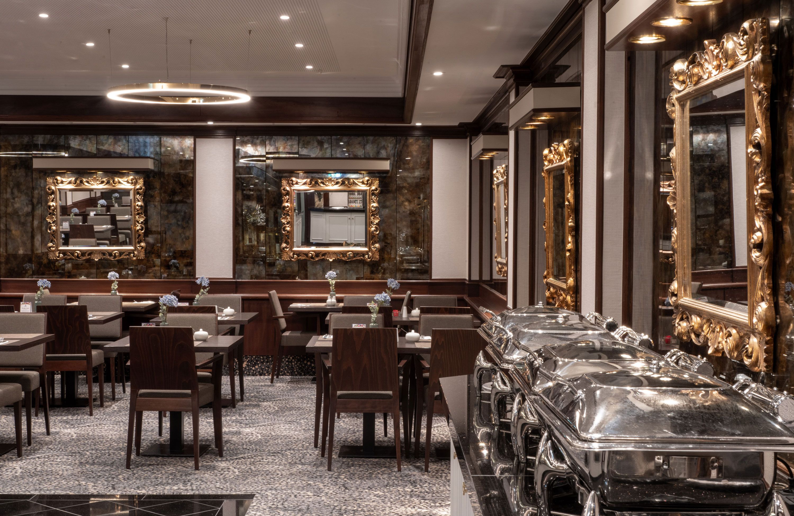 A hotel dining area with multiple tables and chairs, large mirrors, and a buffet station.
