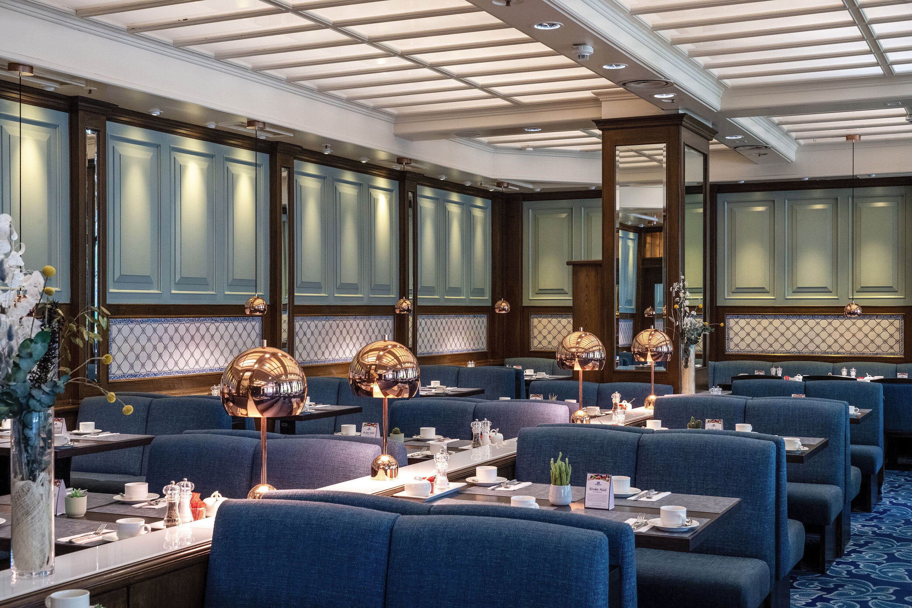 A dining area with blue upholstered booths, tables set with white tableware, and decorative lamps.