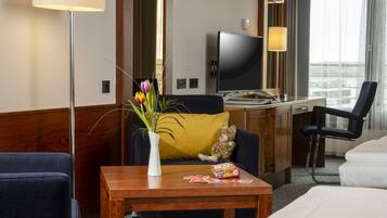 A hotel room with a bed, a desk, a chair, a television, a lamp, and a vase with flowers.