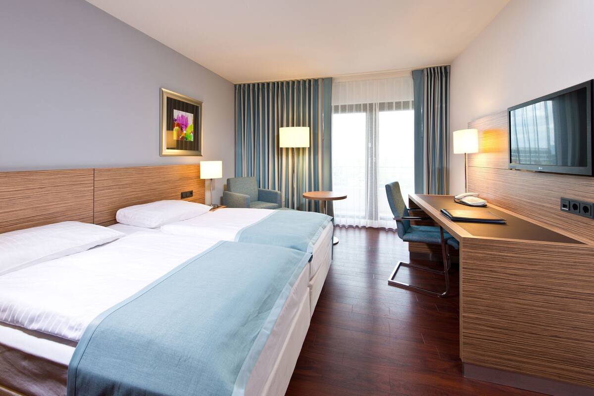 Habitación de hotel con dos camas, un escritorio, una silla, un televisor y una ventana con cortinas.
