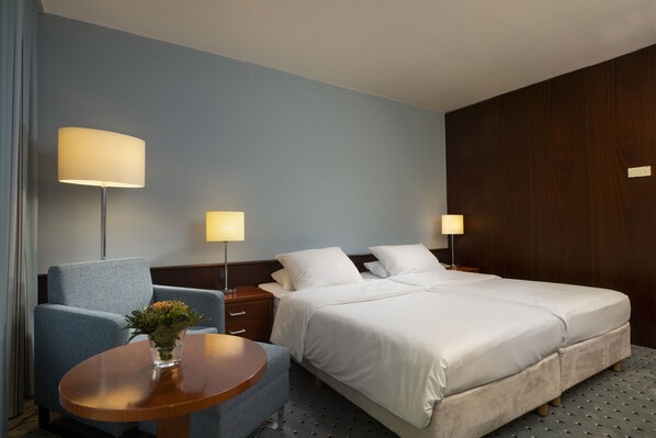 Una habitación de hotel con una cama doble, una silla, una mesita y dos lámparas de noche.