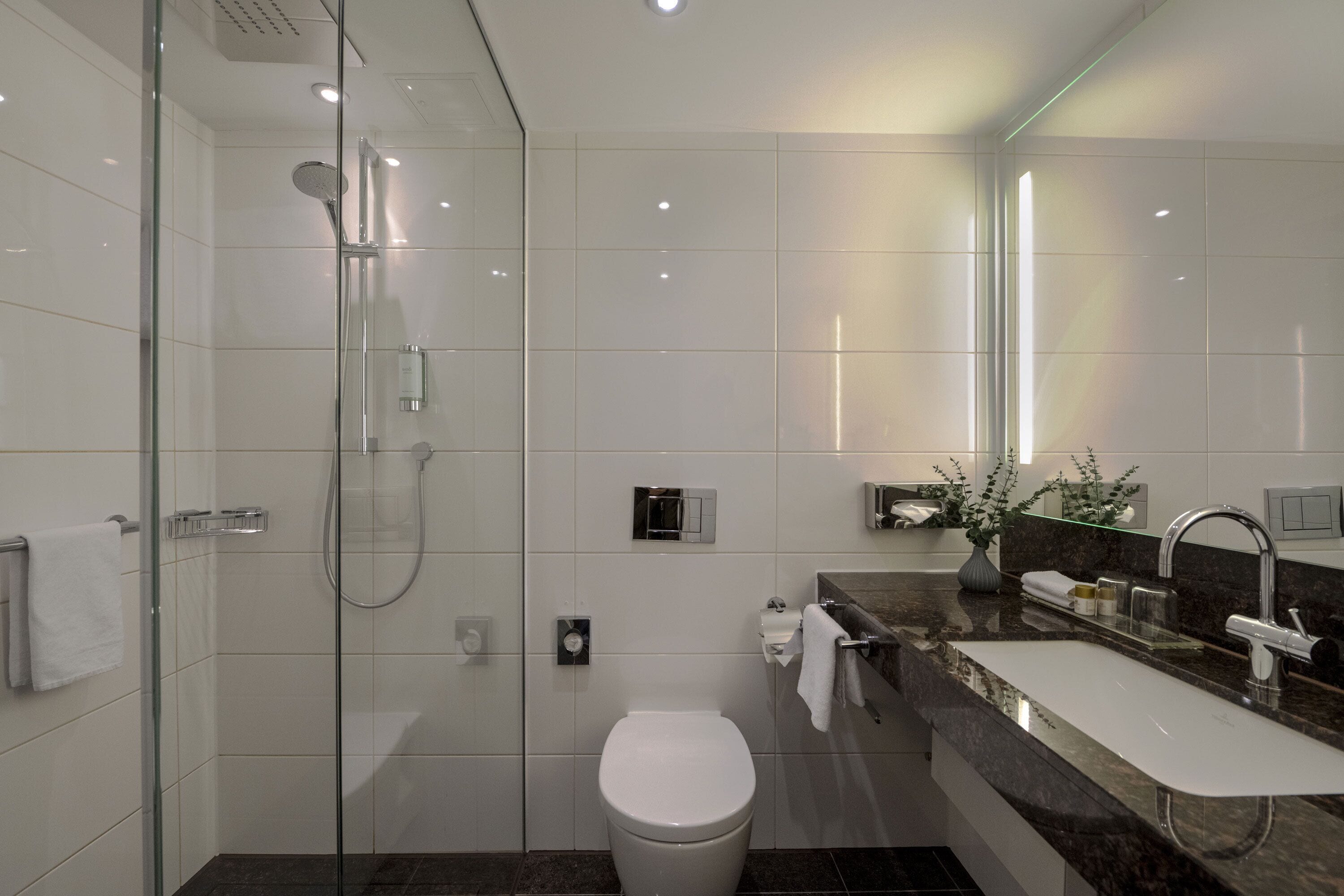 A modern bathroom with a glass-enclosed shower, a white toilet, and a marble sink with a mirror.