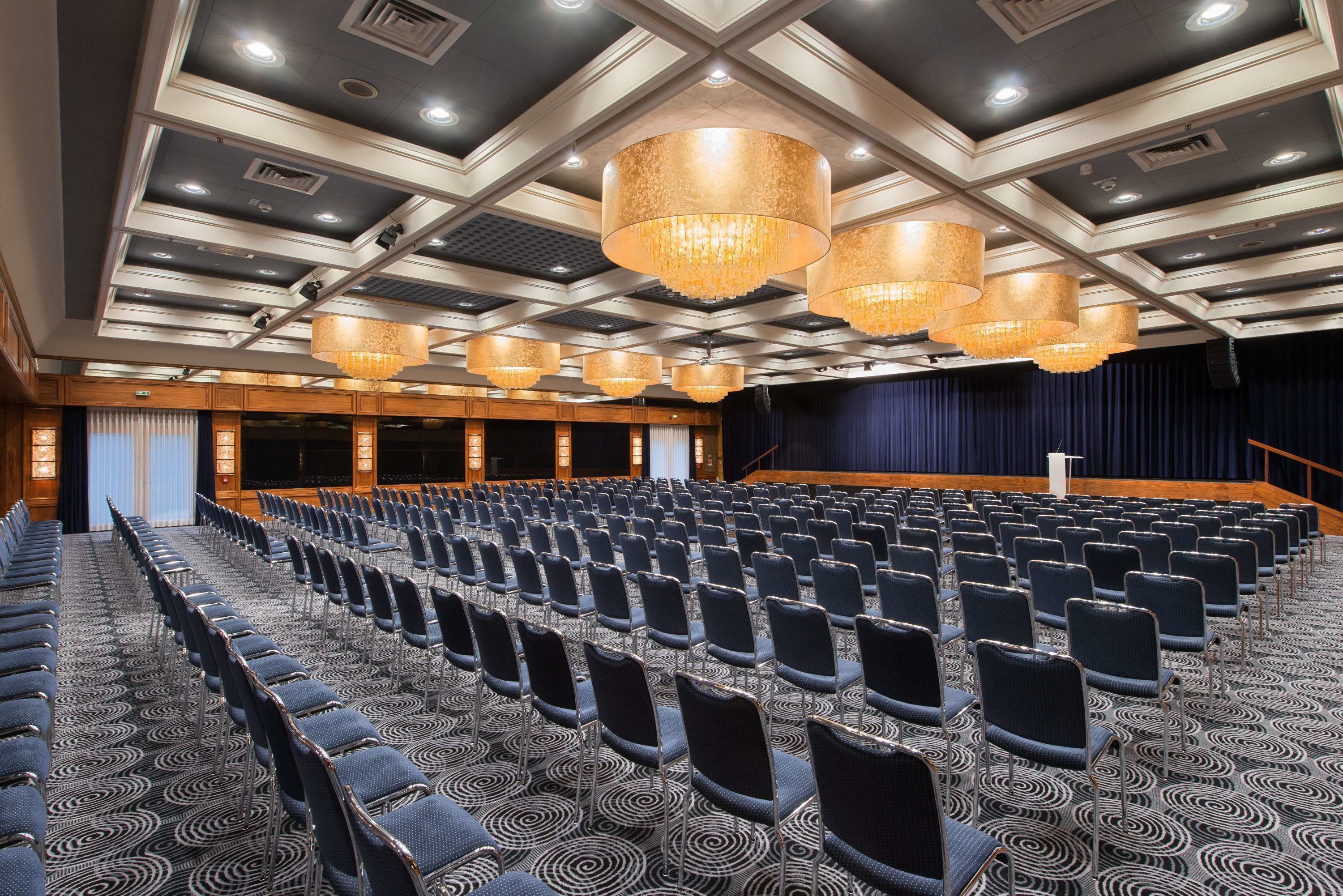 A conference room with rows of chairs, a stage, and large chandeliers.