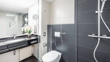 A modern bathroom with a black and white tiled shower, a glass-enclosed toilet, and a vanity with a sink and mirror.