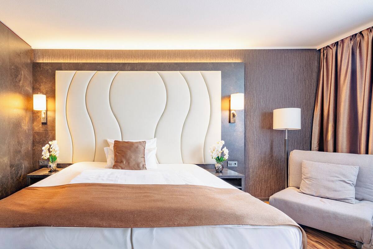 A modern hotel room with a large bed, a sofa, and a wall-mounted headboard.