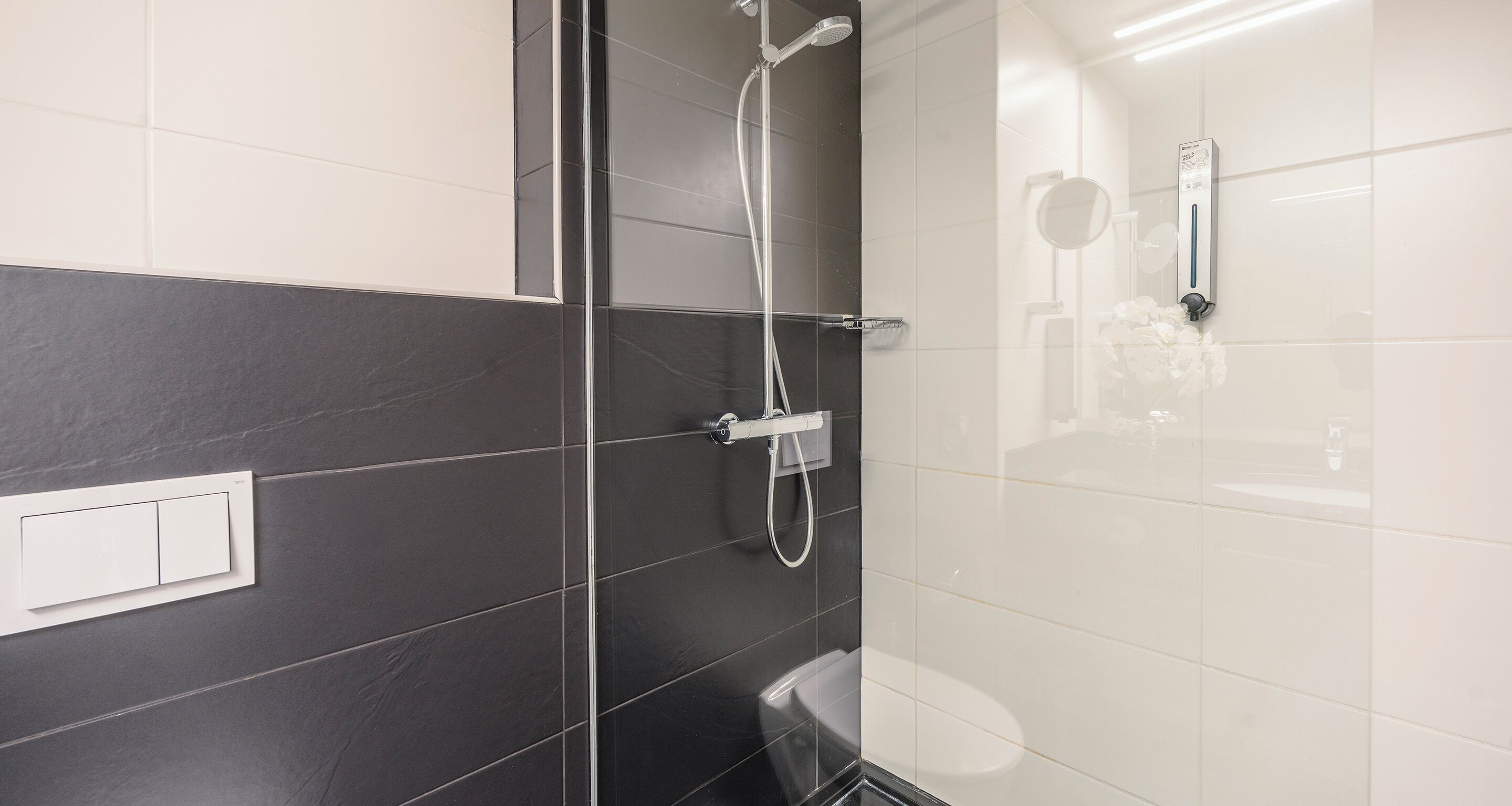 A modern bathroom with a glass-enclosed shower, a toilet, and a wall-mounted light fixture.
