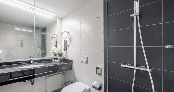 A modern bathroom with two sinks, a large mirror, a shower, and a toilet.