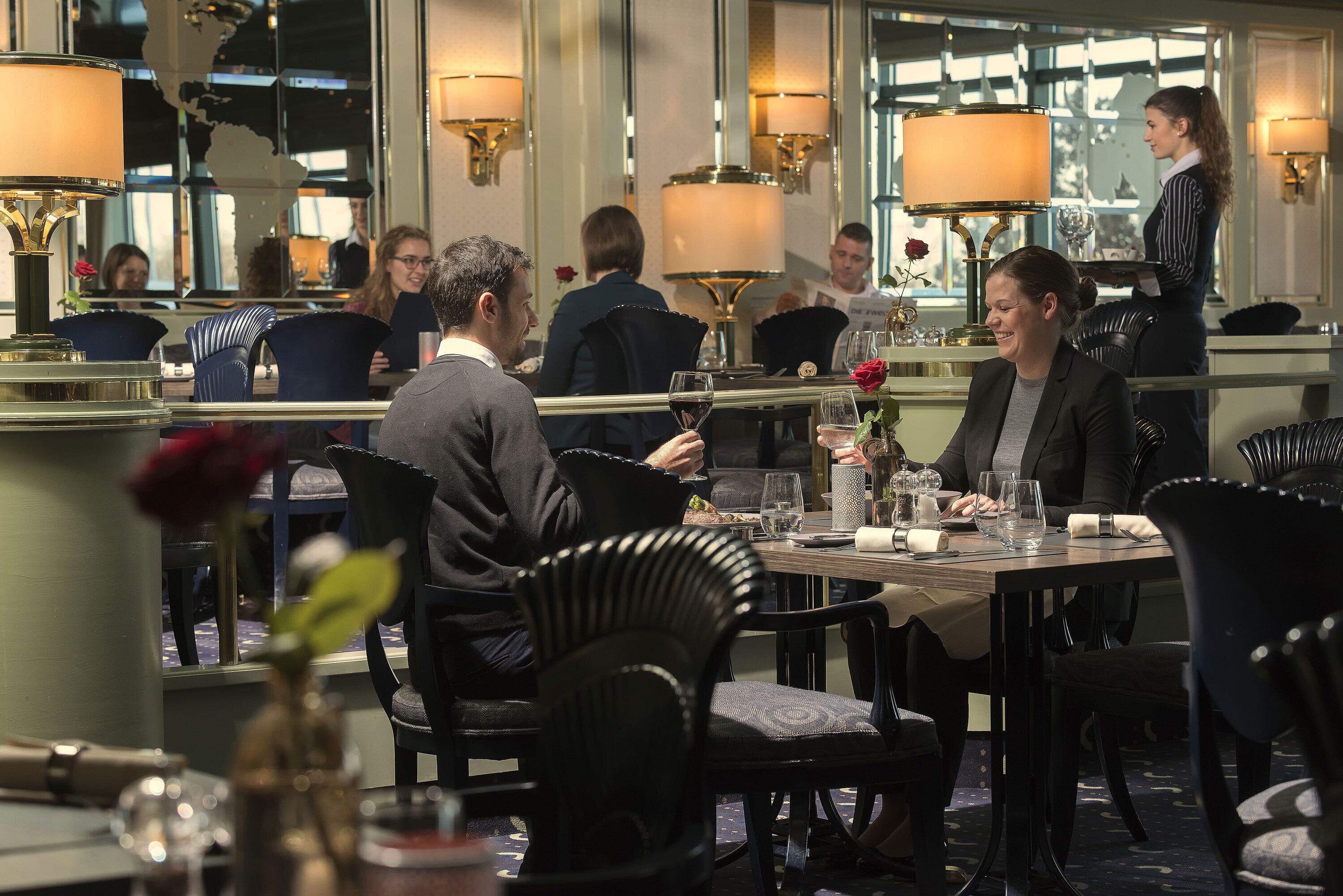 A restaurant with tables set for dining, a waiter attending to guests, and a bar area.