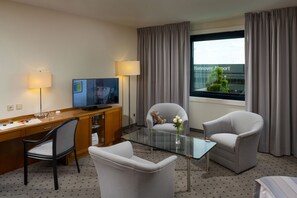 A hotel room with a desk, two chairs, a television, and a view of the airport.