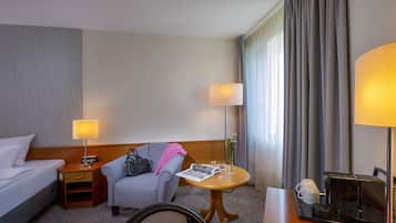 Une chambre d’hôtel comprenant un lit, un bureau avec une machine à café, une chaise, une table avec un magazine et une lampe.
