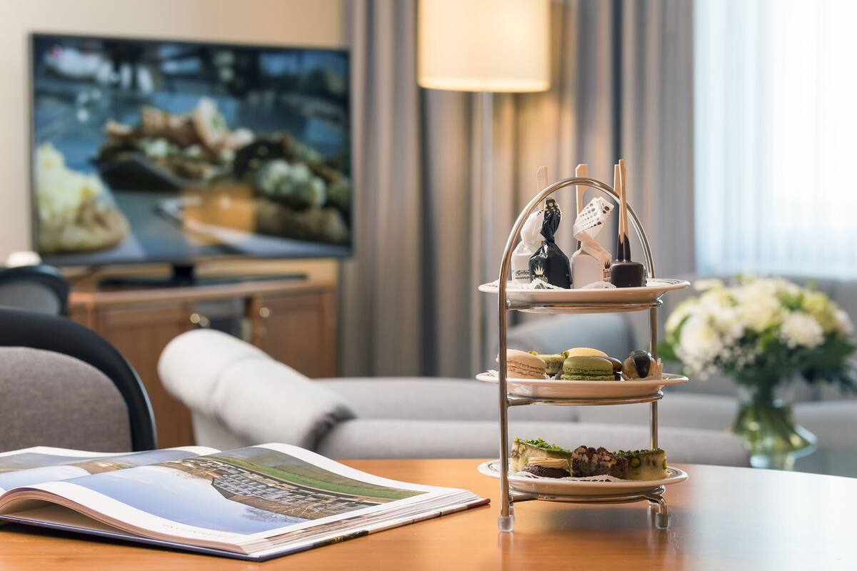 A three-tiered dessert stand with pastries on a table in a hotel room.
