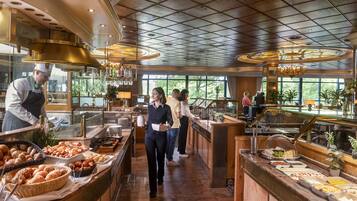 Zona de bufé con diferentes opciones de comida, un cocinero preparando alimentos y un bar con un bartender.