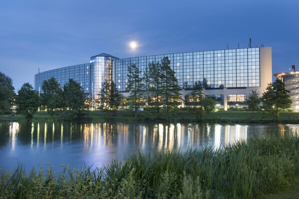 A modern hotel with a glass facade, a reflection in the water, and a moon in the sky.