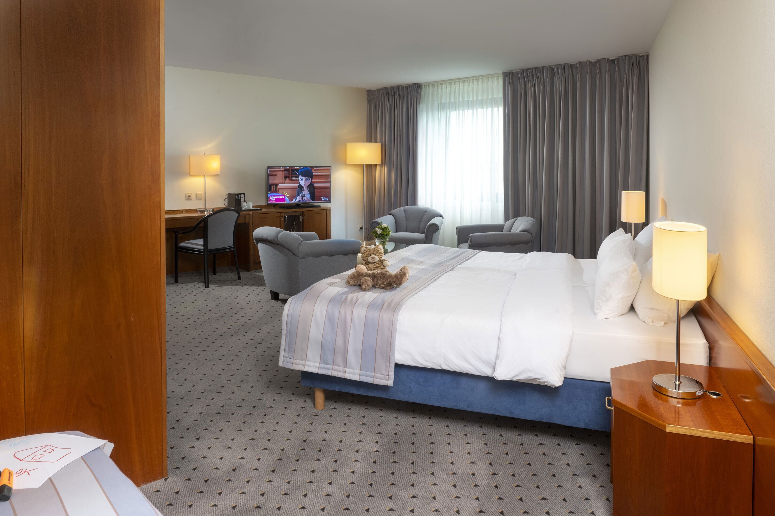 Una habitación de hotel con una cama, dos sillones, un escritorio con computadora y televisión.