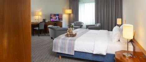Una habitación de hotel con una cama, dos sillones, un escritorio con computadora y televisión.
