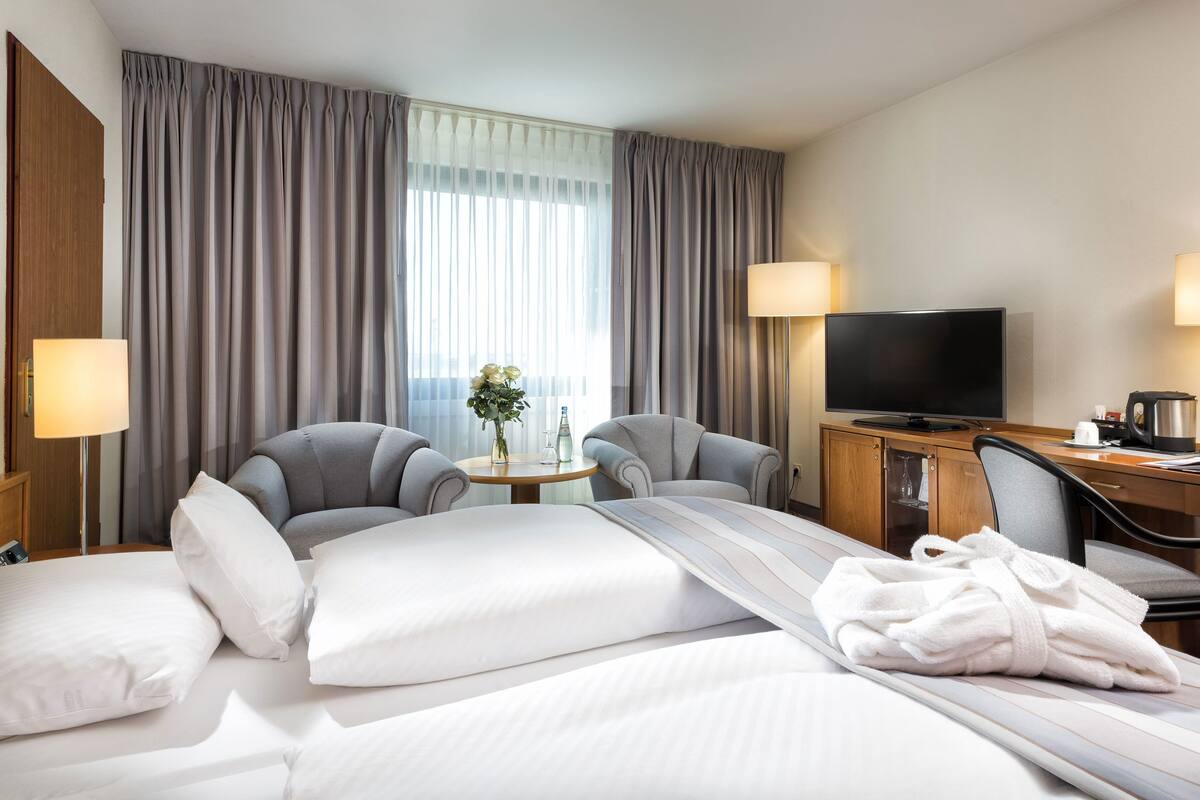 A hotel room with a bed, two armchairs, a desk with a TV, a coffee maker, and a lamp.
