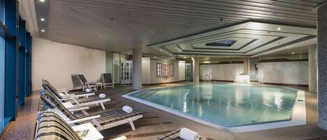 A swimming pool area with lounge chairs and a ceiling with a geometric design.