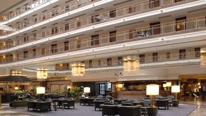 Un vestíbulo de hotel de varios niveles con una zona de estar central, varios pisos con balcones y un mostrador de recepción.