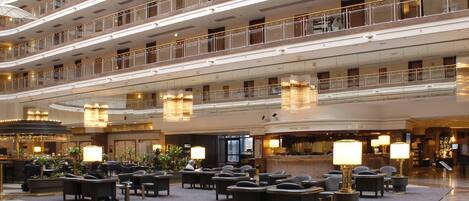 Un hall d’hôtel à plusieurs niveaux, doté d’un espace salon central, de plusieurs étages avec balcons et d’un comptoir d’accueil.