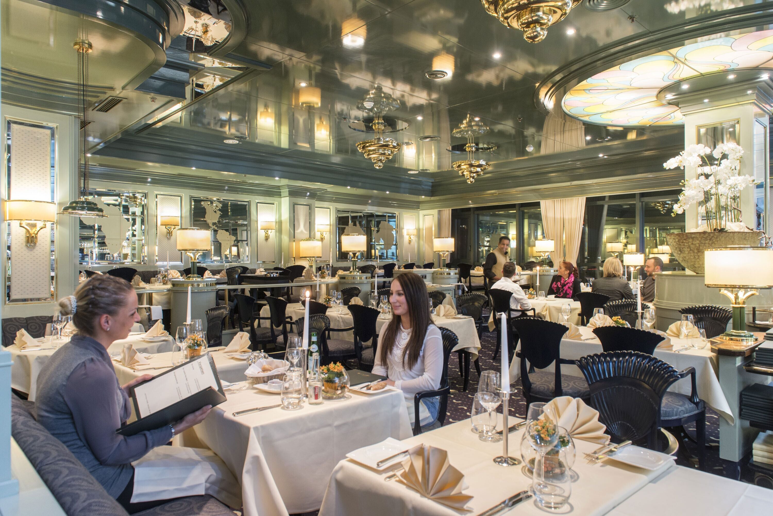 A formal dining area with multiple tables, candles, and chandeliers.