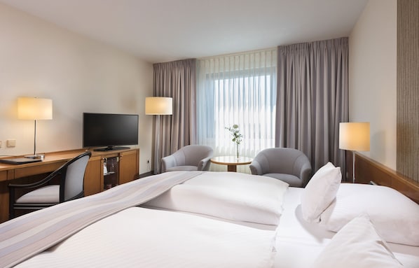 Habitación de hotel con cama, dos sillones, escritorio con televisor y una pequeña mesa con planta.