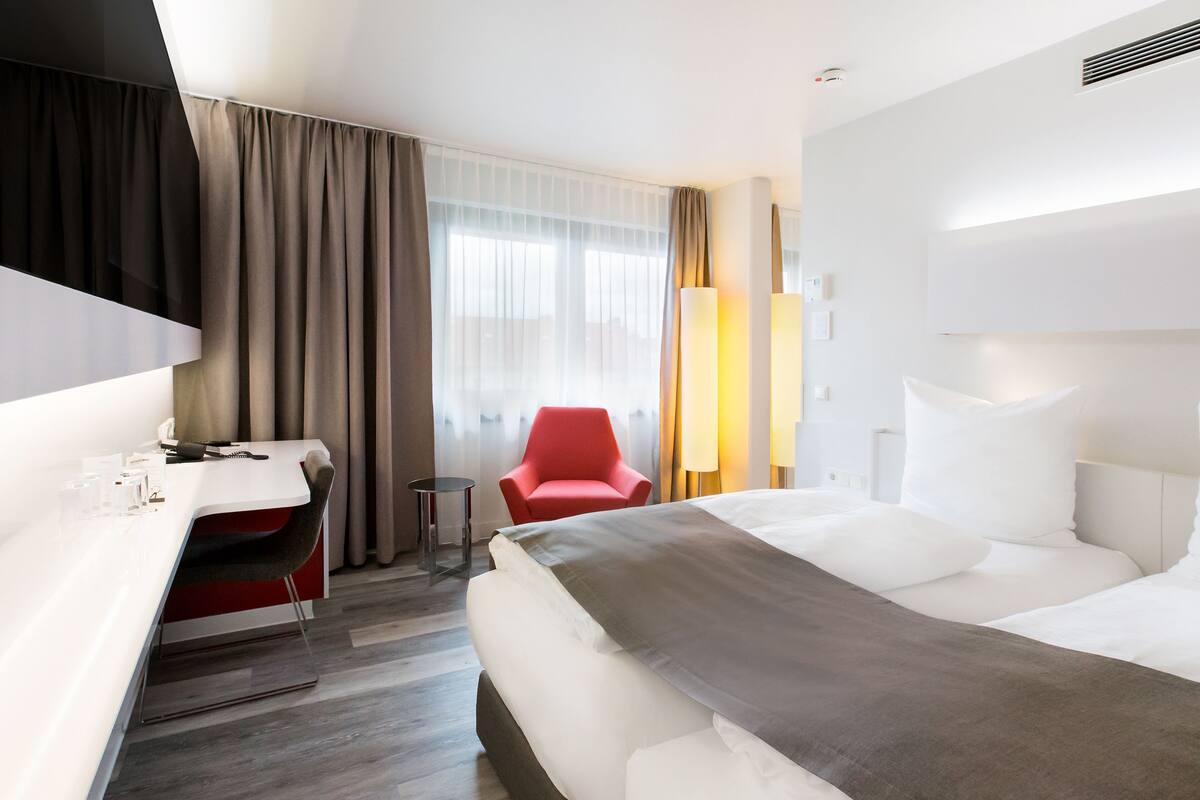 A modern hotel room with a bed, a desk, a chair, and a TV.