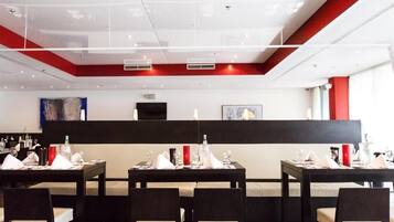 Un restaurant modern amb taules preparades per sopar, una barra negra i obres d'art a les parets.