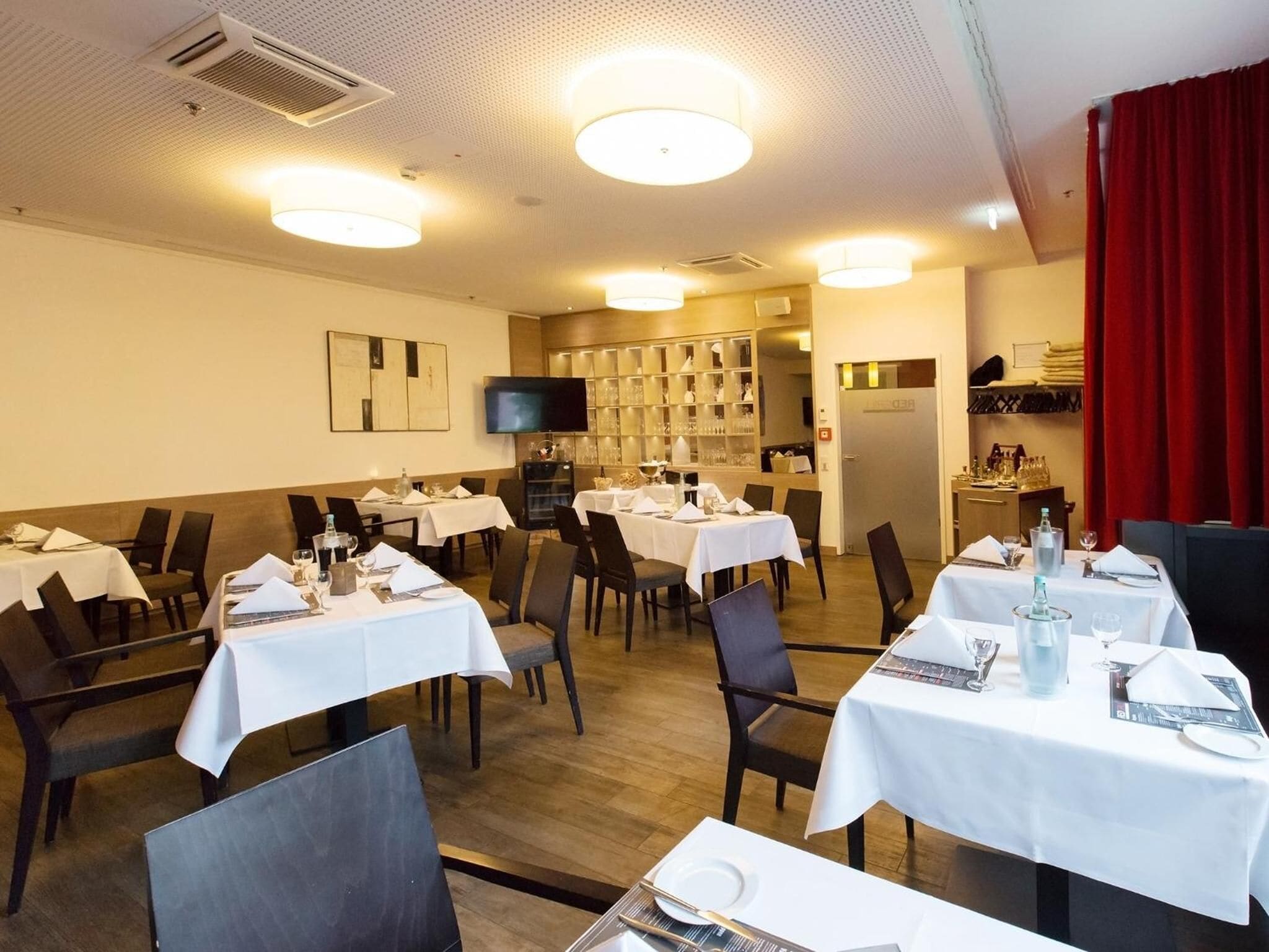 A restaurant with multiple tables set for dining, a television screen, and a wine rack.