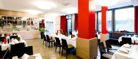 Un restaurante moderno con mesas blancas y detalles rojos, que presenta un suelo de madera y ventanas amplias.