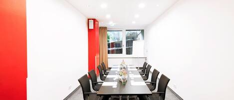 A conference room with a long table, black chairs, and a red accent wall.