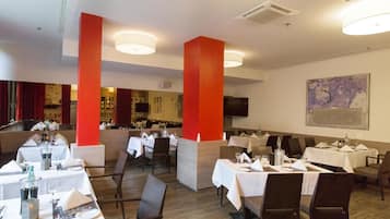 Ein Restaurant mit mehreren Tischen, einer Bar und einem an der Wand befestigten Fernseher.