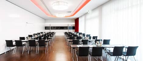 A spacious conference room with rows of tables and chairs, large windows, and a modern chandelier.
