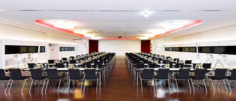 Une grande salle de conférence, avec de nombreuses rangées de tables et de chaises, équipée d’ordinateurs portables et de bouteilles d’eau.