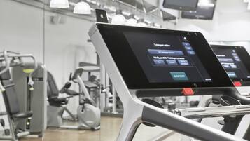 Un gimnasio con equipo de ejercicio y pantallas digitales mostrando programas de entrenamiento.