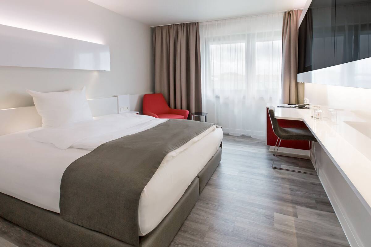 A modern hotel room with a large bed, a desk, a chair, and a TV.
