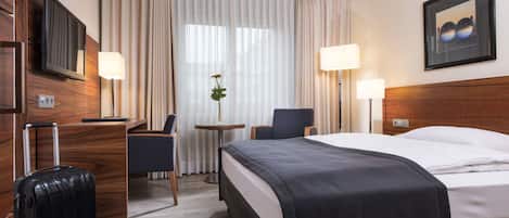 Une chambre d’hôtel avec un lit, un bureau, une chaise, une télévision, une lampe et une valise.