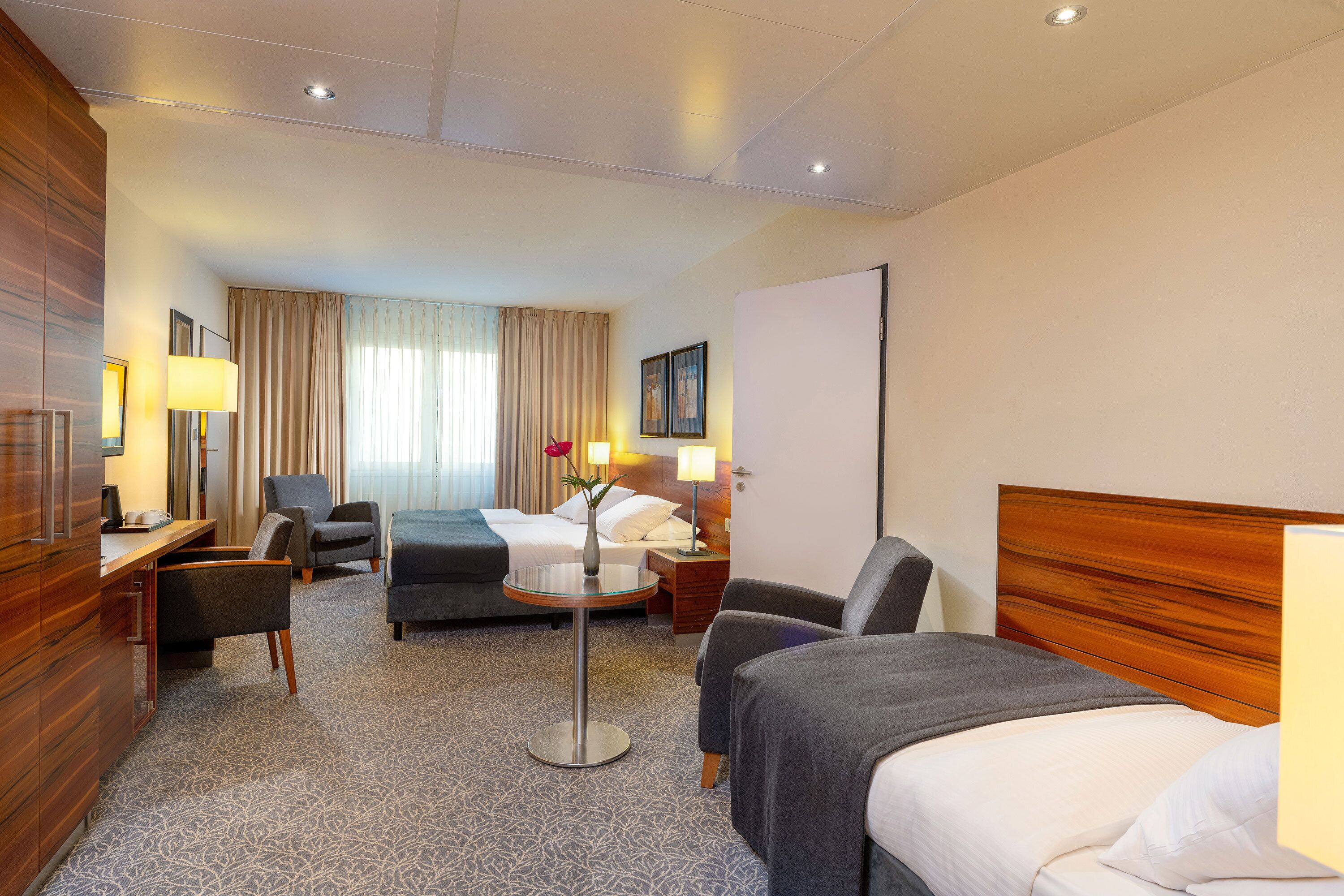 Une chambre d’hôtel comprenant un lit, deux fauteuils, un bureau et une petite table.