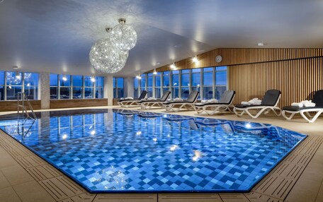 An indoor swimming pool with checkered tiles, lounge chairs, and a large chandelier.