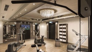 A gym with exercise equipment, a large mirror, and a chandelier. - Maritim Hotel München (Munich)