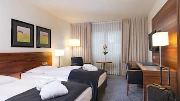 A hotel room with two beds, a desk, a chair, a TV, and a lamp.