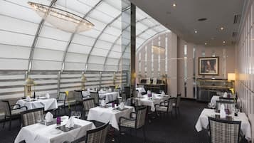 A restaurant with tables set for dining, a bar area, and a large window offering a view.