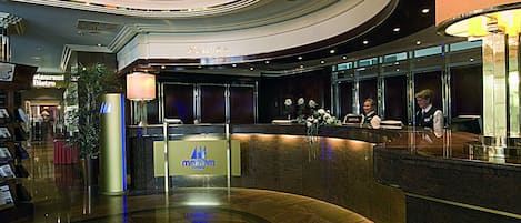 Un moderno vestíbulo de hotel con mostrador de recepción, letrero de restaurante y una gran planta en maceta.