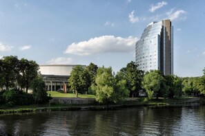 A modern building with a reflective glass facade, a large courtyard with trees, and a body of water in front. - Maritim Hotel Ulm (Ulm)