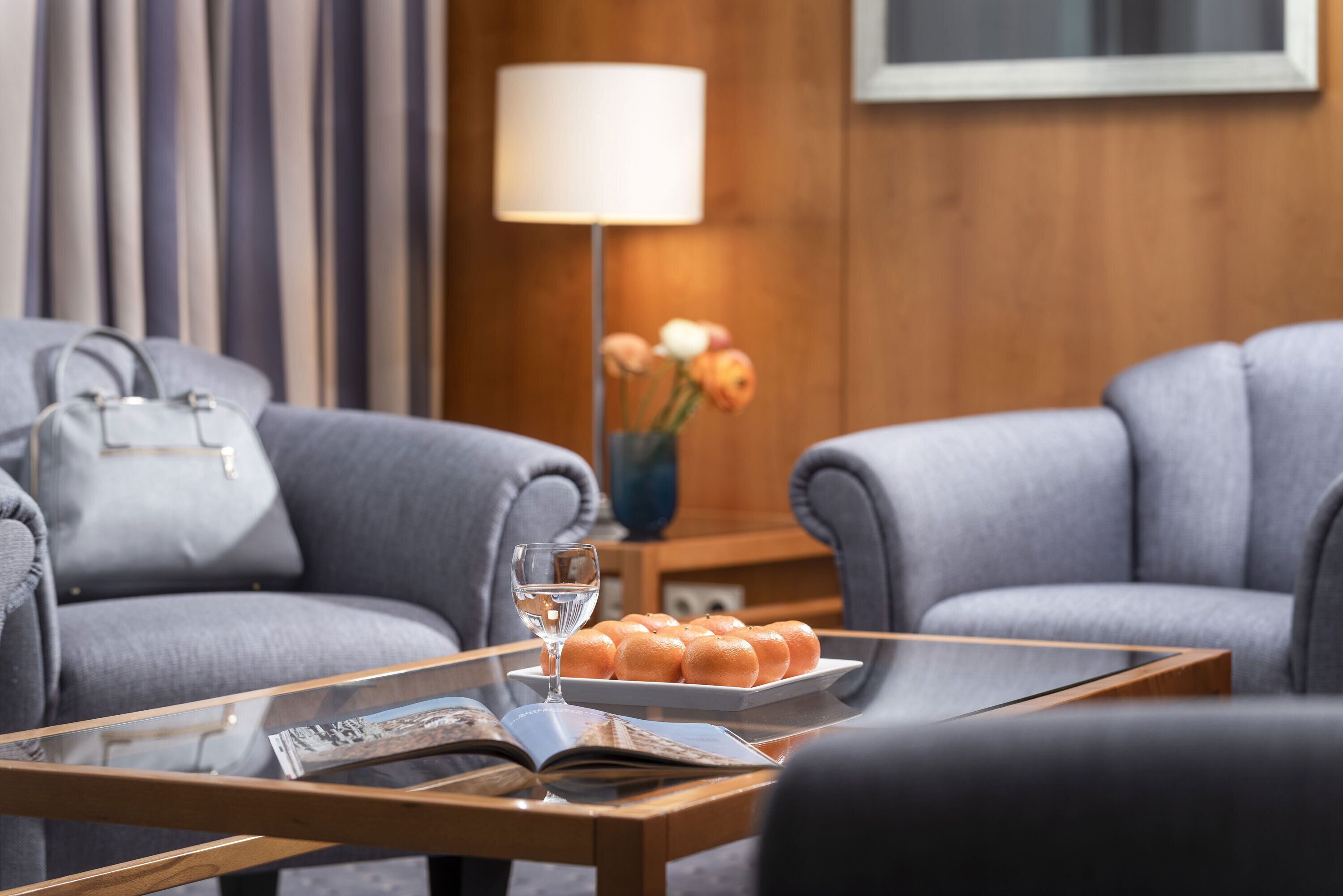 A modern living room with a glass coffee table, a sofa, a lamp, and a vase with flowers.