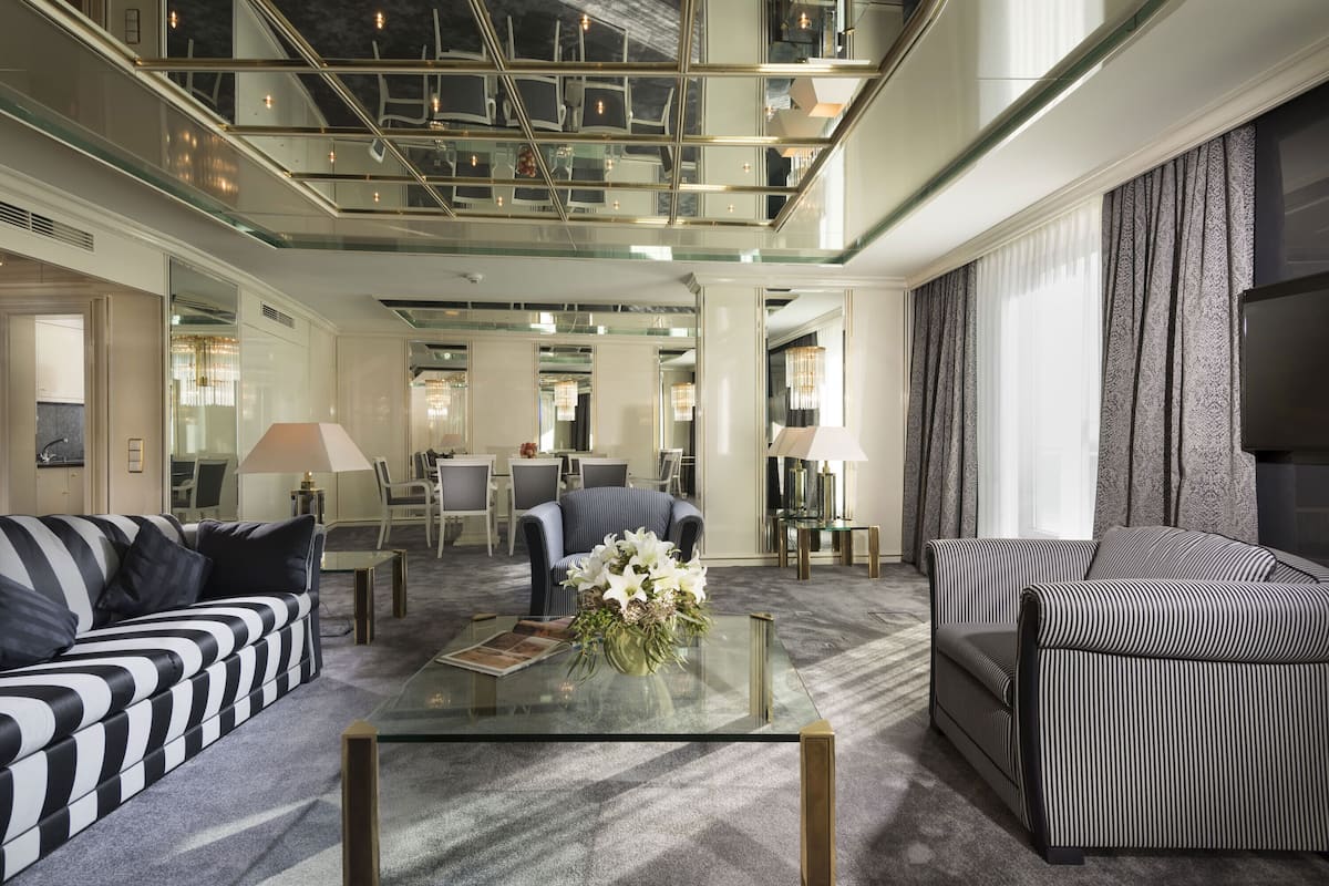 A spacious lobby with a high ceiling, a glass coffee table with a floral centerpiece, striped sofas, and a dining area in the background.